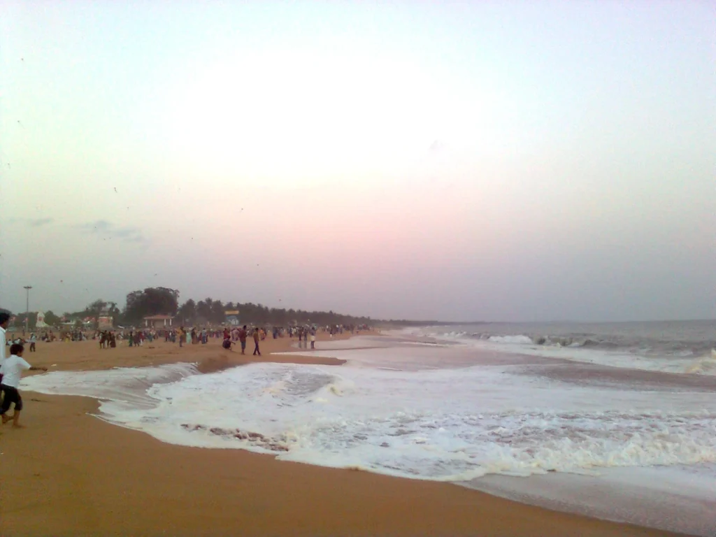 Kollam Beach with waves rolling onto the sandy shore and visitors enjoying the beach on a cloudy day.