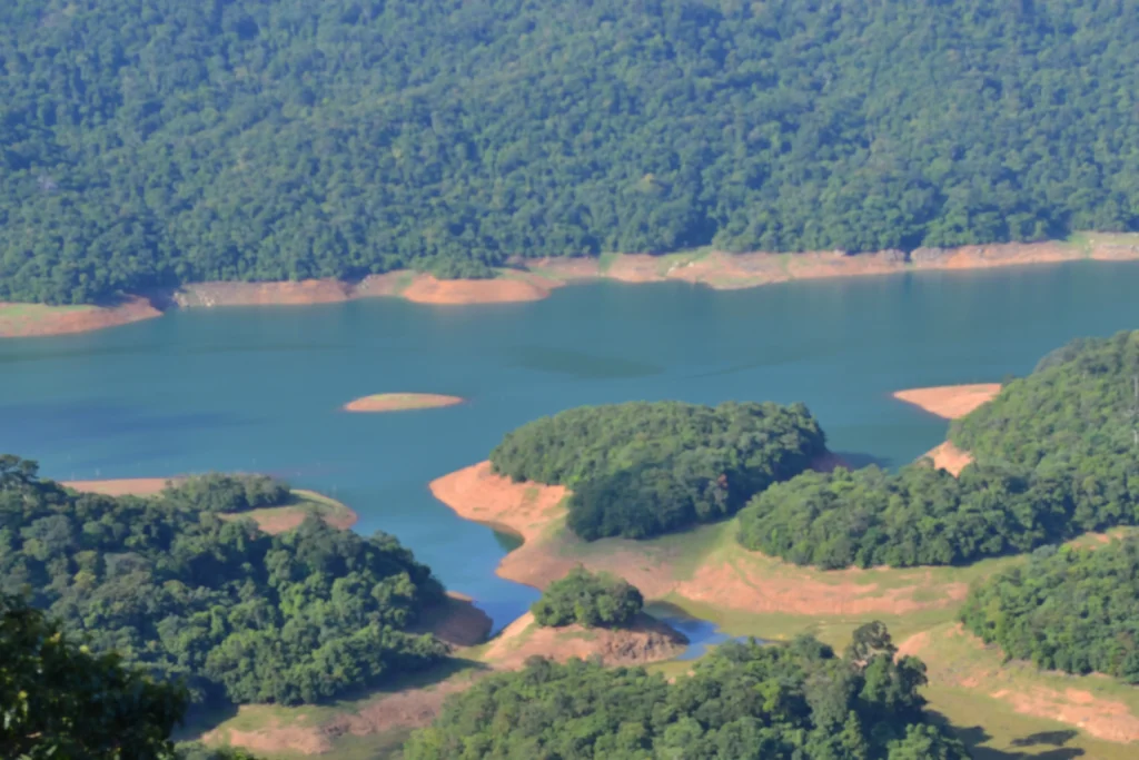 Scenic aerial view of Thenmala Dam and reservoir in Kollam, surrounded by lush green forested hills and small tree-covered islands.